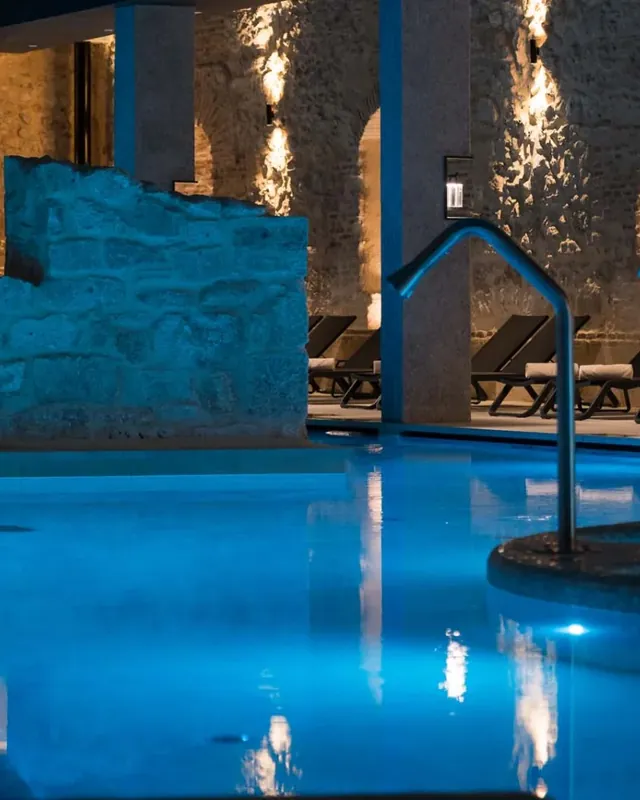 La piscina termal iluminada de azul junto a los muros antiguos